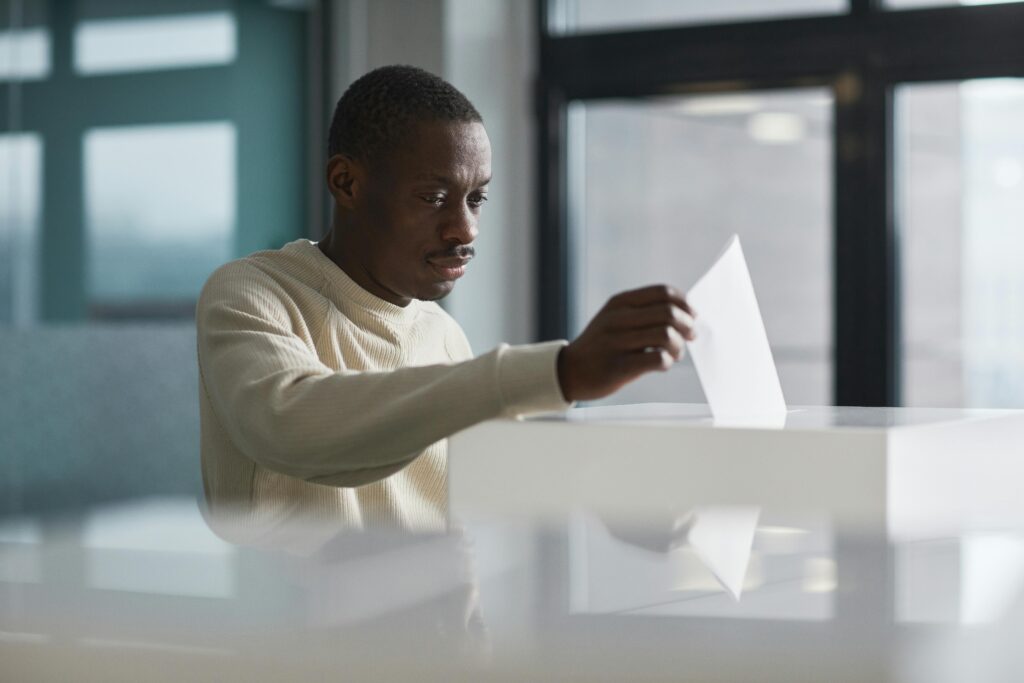 A young man casting his vote at an indoor polling station, focused on the democratic process.