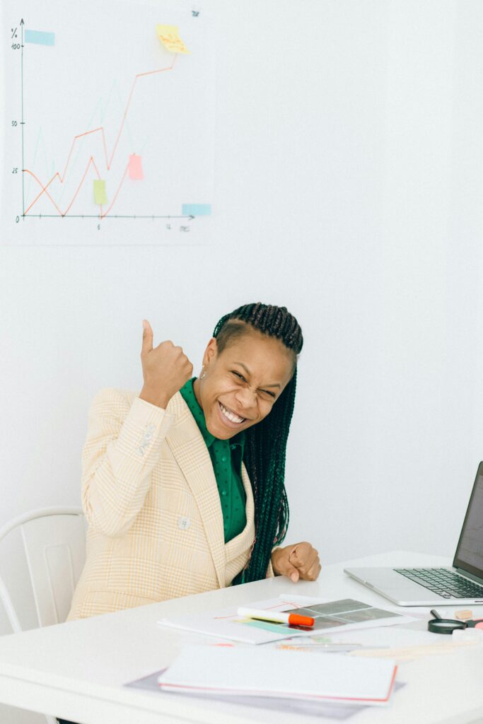 Smiling businesswoman gives thumbs up in an office setting, indicating success and achievement.